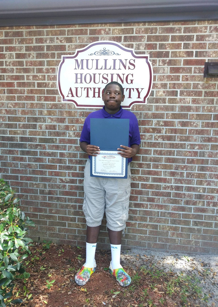 Joshua Brigman stands outside of Mullins Housing Authority, proudly holding his What Home Means to Me winning certificate. 